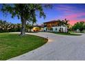 Beautiful exterior elevation of the home with a large tree and circular driveway at dusk at 1208 Oak Hammock Rd, Sarasota, FL 34240
