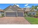 This house features a brick driveway, a two-car garage, manicured lawn, and tropical plants at 11176 Roseate Ct, Sarasota, FL 34238