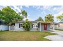 Quaint single-story home with a red door and a covered porch, surrounded by lush greenery and a well-kept lawn at 3515 W Pearl Ave, Tampa, FL 33611