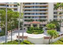 Elegant condo entrance with a covered porte-cochere, lush landscaping, and circular driveway at 3030 Grand Bay Blvd # 323, Longboat Key, FL 34228