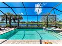 A screened-in pool with a hot tub overlooks a serene lake and beautiful palms under a clear blue sky at 19921 Petrino St, Venice, FL 34293
