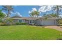 Single-story home featuring an attached two-car garage, a well-manicured lawn, and lush tropical landscaping at 452 Picasso Dr, Nokomis, FL 34275