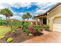 Charming home showcasing a brick driveway, manicured flower beds, and tropical palm trees against a partly cloudy sky at 10111 Malachite Dr, Bradenton, FL 34211