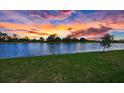 Scenic view of a calm lake reflecting a vibrant sunset, framed by lush green grass at 10217 Canaveral Cir, Sarasota, FL 34241