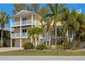 Charming yellow two-story home featuring double balconies, two-car garage, and lush tropical landscaping at 306 Poinsettia Rd, Anna Maria, FL 34216