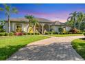 Single-story home featuring a well-manicured lawn, lush landscaping, and a circular brick driveway at 7408 S Serenoa Dr, Sarasota, FL 34241