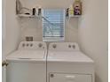 Bright laundry room with a window, shelving, and a modern white washer and dryer at 5547 Logan Cave Ave, Wimauma, FL 33598