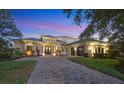 Beautiful home with manicured lawn, arched windows, tile roof, and brick driveway at dusk at 3432 Founders Club Dr, Sarasota, FL 34240