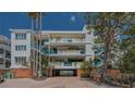 Condo building with blue railings, lush landscaping, and brick driveway leads to covered parking area at 340 Gulf Of Mexico Dr # 136, Longboat Key, FL 34228