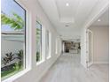 Bright hallway featuring tray ceilings, natural light, and views of the kitchen. Light wood-look tile flooring throughout at 6028 Cat Claw Ln, Bradenton, FL 34210