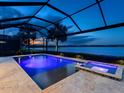 Stunning screened pool at dusk featuring ambient lighting, a spa, and serene lake views at 7864 Grande Shores Dr, Sarasota, FL 34240