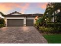 Attractive home with a two-car garage, brick driveway, and tropical landscaping under a vibrant sunset at 3512 Scrub Creek Run, Lakewood Ranch, FL 34211