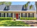 Home with dormer windows, black shutters, a brick walkway, red front door, and green shrubbery at 5504 Beneva Woods Circle, Sarasota, FL 34233