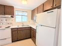 A cozy kitchen featuring wood cabinetry, a double basin sink beneath a window, and white appliances at 5901 Garden Ln # H23, Bradenton, FL 34207