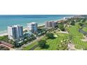 Expansive aerial view showcasing beachfront condos alongside a lush green golf course and ocean at 675 Longboat Club Rd # 23A, Longboat Key, FL 34228