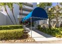 Exterior of condo building with a blue awning over entrance and mature trees surrounding at 1000 Riverside Dr # B501, Palmetto, FL 34221