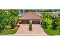 Stunning aerial view of a home with a terracotta tile roof, a paver driveway and lush landscaping near a lake at 213 Babbling Brook Run, Bradenton, FL 34212