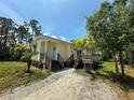 Charming home featuring a light yellow exterior, wooden deck, gravel driveway, and well-maintained landscaping at 8297 Strasse Blvd, Punta Gorda, FL 33982