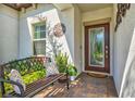 Inviting covered front porch with beautiful brick flooring, a decorative glass front door, and a comfortable bench at 17578 Holly Well Ave, Wimauma, FL 33598