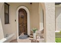 Arched wood front door with brick pavers and lush plants by a white wicker chair at 5624 Aaron Ct, Sarasota, FL 34232