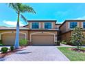 A beautiful two-story home featuring an attached two-car garage, a brick paved driveway, and lush green landscaping at 6406 Grand Estuary Trl # 102, Bradenton, FL 34212