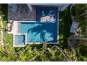 Aerial view of a serene pool and spa area surrounded by lush greenery, stone pavers, and modern furniture at 222 Willow Ave, Anna Maria, FL 34216