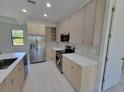 Modern kitchen boasts stainless steel appliances, quartz countertops, light wood cabinets, and sleek tile backsplash at 5115 Foxhall Rd, North Port, FL 34288