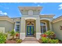 Elegant front entrance with a light green exterior, arched doorway, blue double doors, and lush tropical landscaping at 12311 Newcastle Pl, Lakewood Ranch, FL 34202