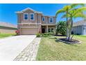 Exterior elevation of a tan two-story home with a lush front yard, long driveway, and a two-car garage at 7822 110Th E Ave, Parrish, FL 34219