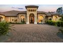 Close-up of a custom home with a grand arched entrance, terracotta roof, brick driveway, and manicured landscaping at 20706 79Th E Ave, Bradenton, FL 34202