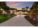 Home exterior featuring a paved driveway, lush landscaping, and mature trees, and a colorful dusk sky at 3302 Sabal Cove Ln, Longboat Key, FL 34228