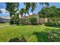 Well-manicured front yard with lush green grass, mature trees, and a glimpse of the charming home at 8005 Royal Birkdale Cir, Lakewood Ranch, FL 34202