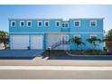 Beautiful two-story home featuring a bright blue exterior, lush landscaping, and a spacious two-car garage at 654 Jungle Queen Way, Longboat Key, FL 34228