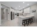 Bright, modern kitchen with white cabinets, stainless steel appliances, a breakfast bar, and wood-look tile flooring at 7743 Nightfall Ter, Sarasota, FL 34241