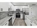 Modern kitchen featuring white cabinets, stainless steel appliances, granite countertops, and a stylish backsplash at 8304 Fishhawk Ave, New Port Richey, FL 34653