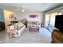 Bright living room with tile floors, floral sofas, ceiling fan, and sliding glass doors to the balcony at 3447 Clark Rd # 246, Sarasota, FL 34231