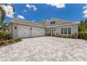Beautiful home exterior featuring a three-car garage, gray brick driveway, and lush landscaping at 8133 Grande Shores Dr, Sarasota, FL 34240