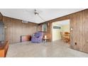 Retro living room featuring classic wood paneling, terrazzo flooring, a ceiling fan, and direct access to dining area at 6628 Auburn Ave, Bradenton, FL 34207