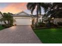 Charming single-story home featuring a manicured lawn, paver driveway, and lush landscaping with elegant exterior lighting at 13848 American Prairie Pl, Lakewood Ranch, FL 34211