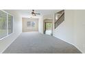 Bright living room with neutral carpet, ceiling fan, staircase, and ample natural light from large windows at 3303 Pine Top Dr, Valrico, FL 33594