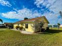 This property features a well-maintained lawn and garden and a yellow exterior under a partly cloudy sky at 6113 Mckee St, Port Charlotte, FL 33981