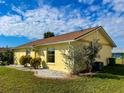 This property features a well-maintained lawn and garden and a yellow exterior under a partly cloudy sky at 6113 Mckee St, Port Charlotte, FL 33981