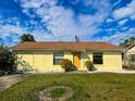 Charming single-story home with a yellow exterior, well-maintained lawn and a brown roof under a partly cloudy sky at 6113 Mckee St, Port Charlotte, FL 33981