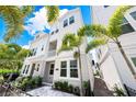 Low angle of a three-story townhome with white siding and tropical landscaping at 2408 Ezzell Ct, Sarasota, FL 34237