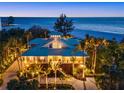 Stunning beachfront home with lush landscaping, palm trees, and breathtaking ocean views at twilight at 26 Sandy Hook S Rd, Sarasota, FL 34242