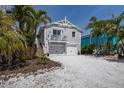 Inviting two-story coastal home featuring white gravel driveway, tropical palms, and light gray facade at 799 Jacaranda Rd, Anna Maria, FL 34216
