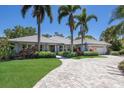 Beautiful single-story home with lush landscaping, palm trees, a paver driveway, and a two-car garage at 1780 Pine Harrier Cir, Sarasota, FL 34231
