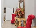 Elegant foyer with decorative mirror, ornate table with floral arrangement, and stylish red armchairs at 5033 Brickwood Rise Dr, Wimauma, FL 33598