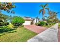 Inviting single-story home with a brick driveway, lush lawn, and mature palm trees at 9022 Coachman Dr, Venice, FL 34293