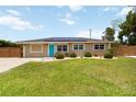 Attractive one-story home featuring a manicured lawn, blue door, solar panels, and privacy fence at 1212 Princeton Ave, Bradenton, FL 34207